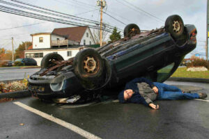 Man lying near a flipped car on the road after a rollover accident in Salt Lake City, Utah. Rollover accident scene showing vehicle damage and potential injury.