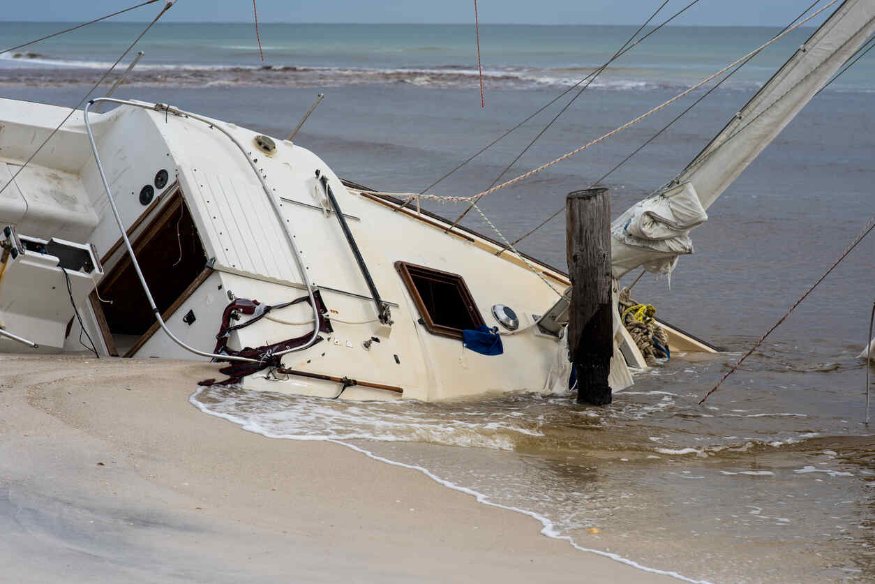 A partially submerged sailboat washed ashore on a sandy beach after a boating accident.