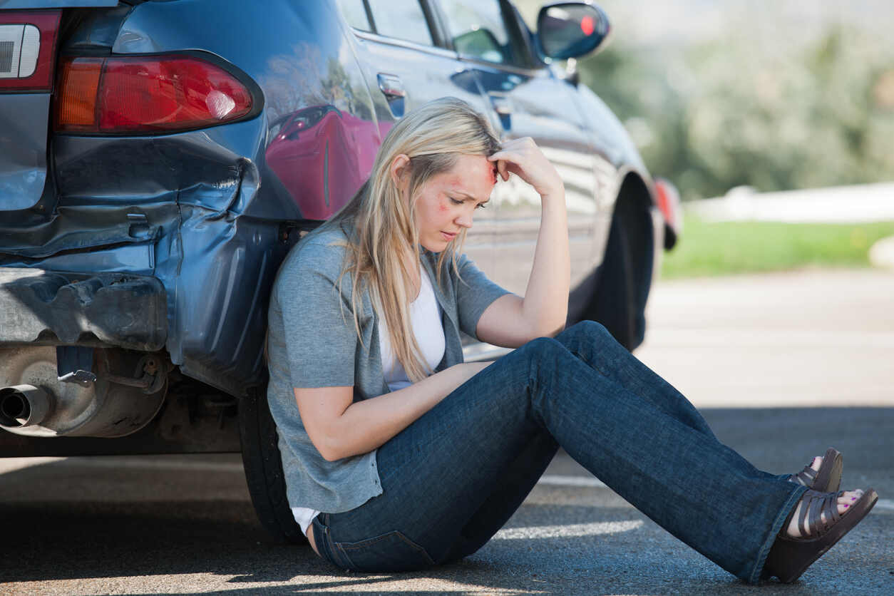 Uninsured and Underinsured car Accident Women sit next to car with sad face.